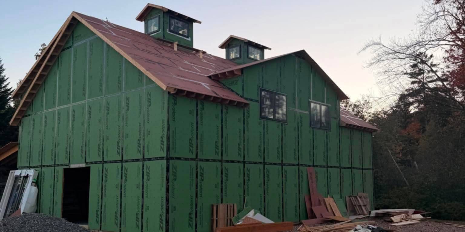 The barn taking shape at dusk, wrapped in green sheathing with two cupolas on the roof
