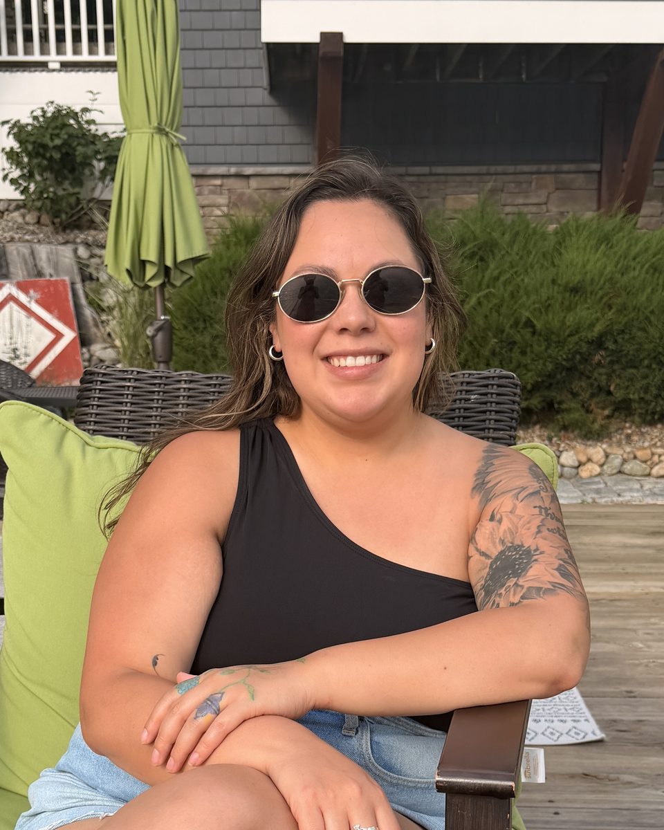 Brittany smiling in a green-cushioned chair on a lakeside deck