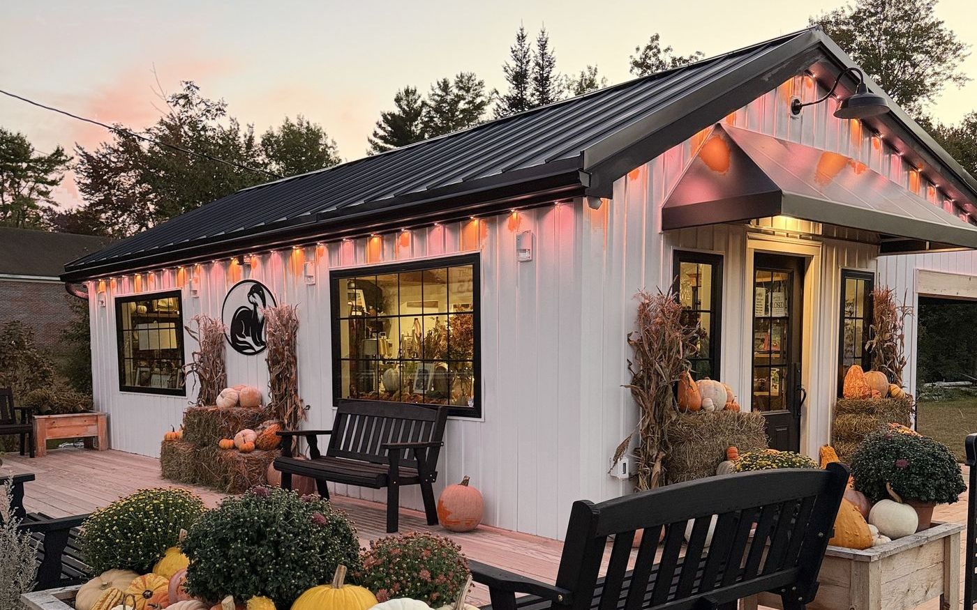 Water's Nook at dusk, glowing with warm lights, with benches on the deck and planters full of fall pumpkins