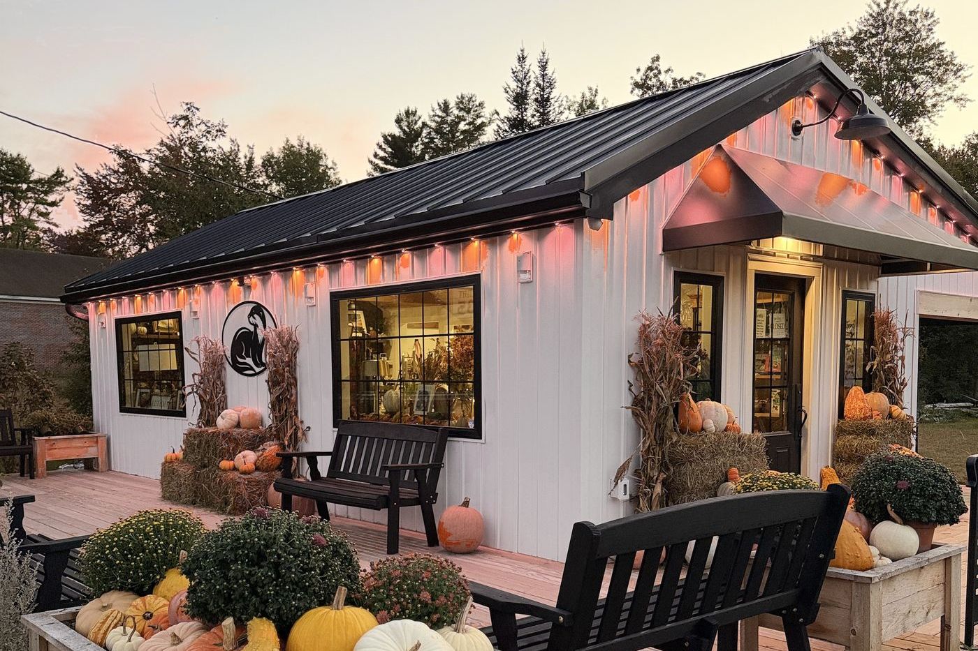 Water's Nook at dusk, glowing with warm lights, with benches on the deck and planters full of fall pumpkins