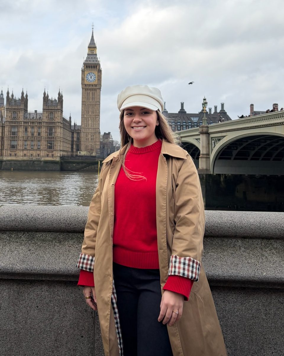 Sienna smiling in a camel trench coat on the Thames, with Big Ben behind her